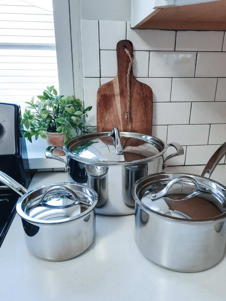 Three stainless steel pots sitting on white counter next to dark wood cutting board and plant 