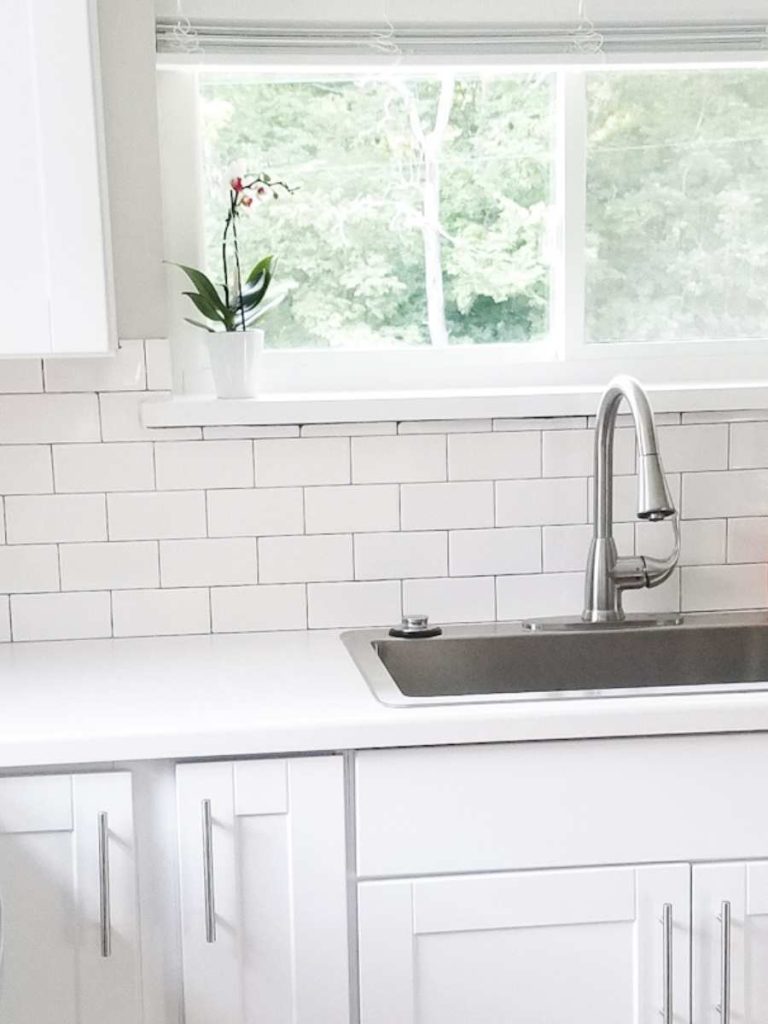 White minimalist kitchen with silver farmhouse sink and white countertops